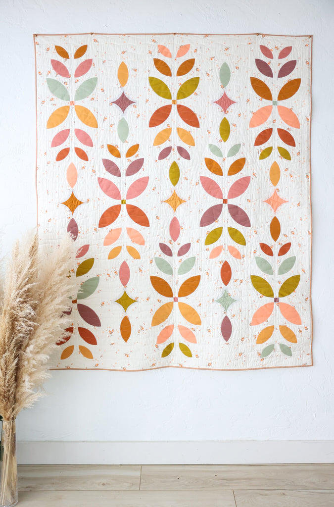 Floral patterned quilt on a white wall with pampas grass. | Flora Fields quilt kit