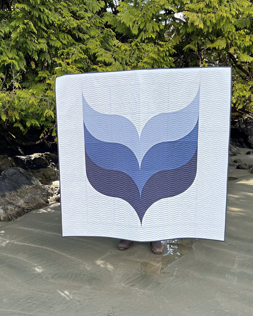 Person holding a quilt with a blue and gray whale design against a natural background